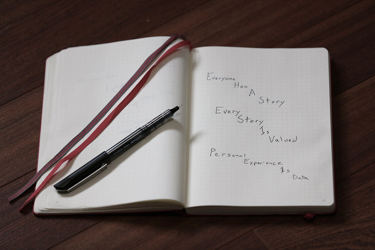 Photograph of a notebook and pen with words: Everyone has a Story; Every Story is Valued; Personal Experience is Data